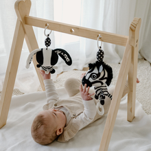 Load image into Gallery viewer, Baby reaching up to play with Ziggy the Zebra and a matching black and white Billie the Bunny toy hanging from a wooden baby gym