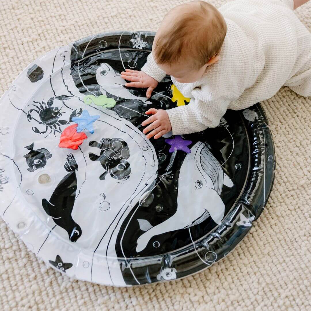 Baby reaching for colourful sea creatures on Young Wonderer's black and white Under the Sea Sensory Water Mat